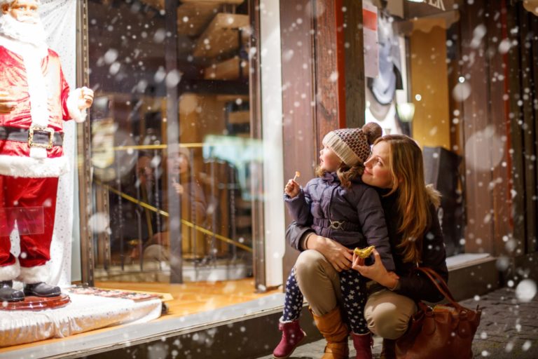 Mother and child looking in window of shop at Christmas with snow